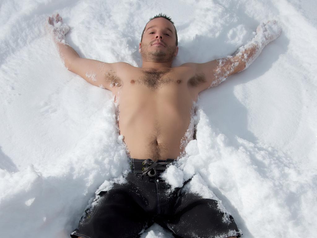 A man makes a snow angel while just wearing shorts