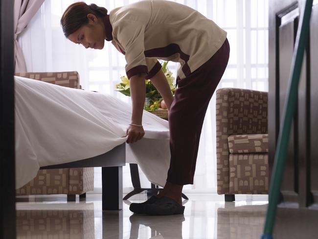 Asian maid tidying up bed and cleaning luxury hotel room