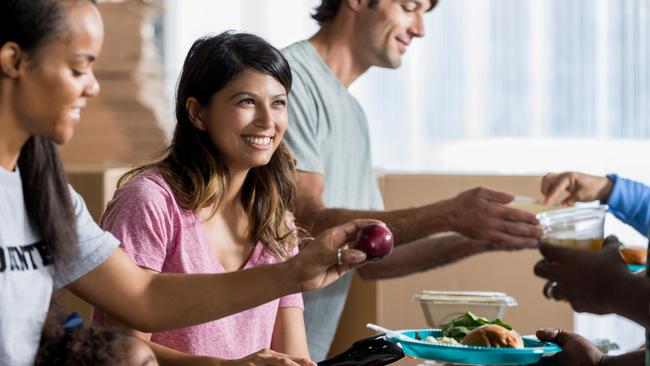 Cheerful mid adult Asian woman smiles while serving food to an unrecognizable person in a homeless shelter. istock