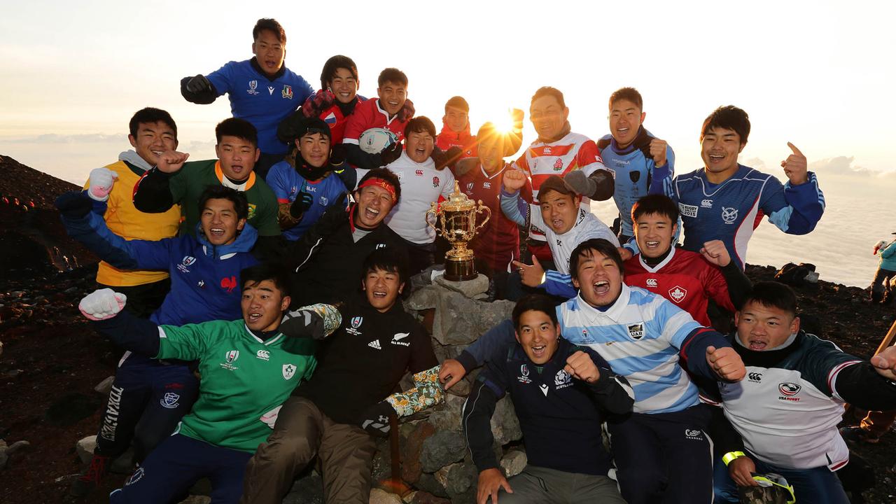 Climbers pose with the Webb Ellis Cup on the summit of Mt. Fuji at sunrise.