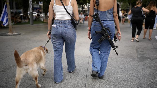 Men and women wielding weapons in civilian clothes have become a common sight. A woman carrying an assault rifle is pictured as she and a friend walk a dog in downtown Tel Aviv. Picture: Getty