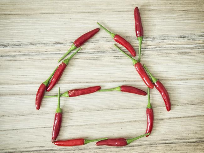 Chili peppers in the house shape on the wooden background.