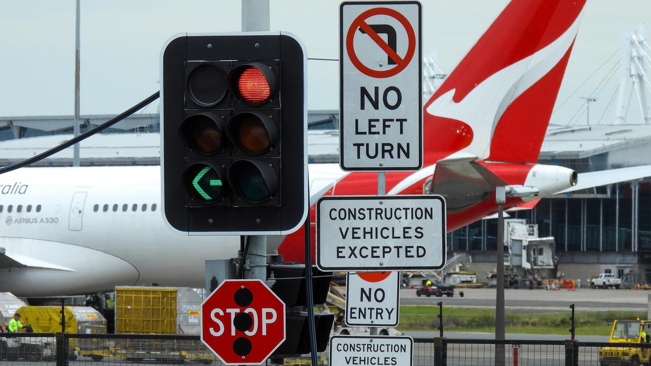 Road signs and traffic lights at the corner of Nigel Love Bridge and Airport Drive, Mascot.  In the background is a Qantas Airbus A330-202 plane, registration VH-EBN, parked on the tarmac of Sydney Kingsford-Smith Airport. In the distance is the domestic terminal.  This image was taken from Nigel Love Bridge, Mascot on a cloudy afternoon on 2 December 2023. Aircraft generic.