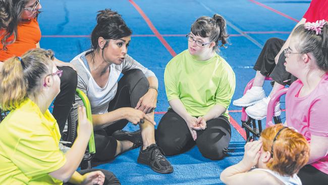 A young woman talking to a group of young girls with disabilities. Home and Community Care services for people with disabilities may be under threat with the NDIS.