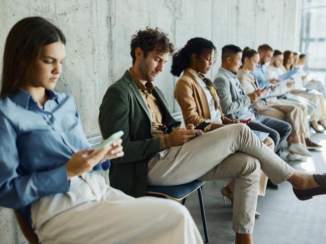 Large group of business people waiting for a job interview in a hallway. Focus is on man using mobile phone.