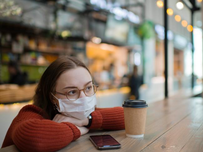 Teenager wearing medical mask protecting herself against virus in a food court of a shopping mall or airport lobby with reusable coffee cup