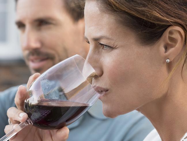 Portrait of young woman drinking red wine while man raising a toast. Mature couple enjoying drinks in the park. Couple enjoying picnic with wine.