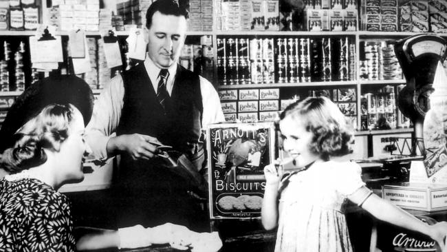 A young child tries an Arnott's milk arrowroot biscuit in a grocery shop in the 1940s. Picture: Handout Historical New South Wales