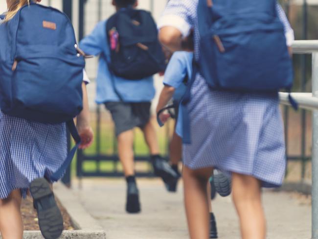 School children running away. They are wearing uniforms and carrying backpacks. They are having a race. Multi ethnic group with Asian, Caucasian and Aboriginal children. Rear view