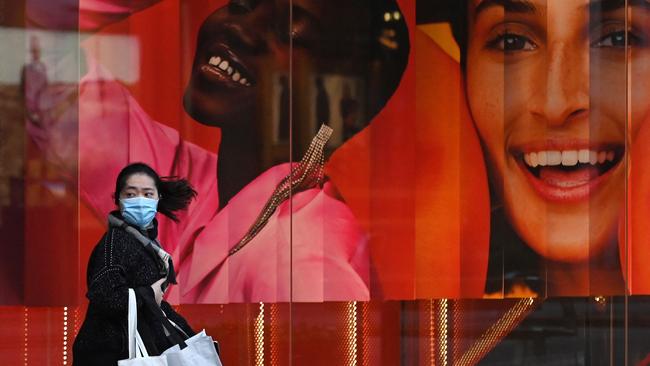 A woman wearing a mask walks past a retail store in Sydney on Saturday after authorities ordered new restrictions. Photo: AFP