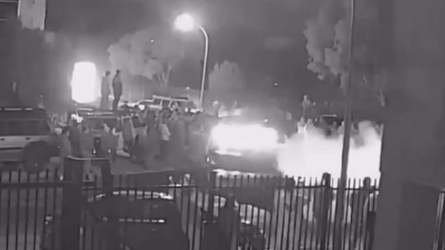 Others stand on the roof of a nearby car to watch on.