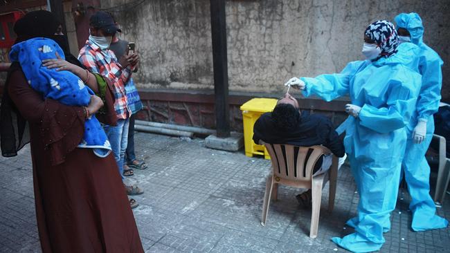 A health worker collects a swab sample from a man as a mother and baby wait at a COVID-19 screening site in Mumbai, India. Picture: AFP