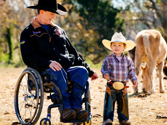 Despite severing his spine and almost losing his life in a bull riding accident, Simon Cresswell pictured with young Colt Cearney, 2, still stages events. Picture: Jonathan Ng