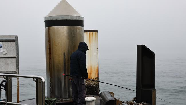 A fisherman is seen on the pier at McMahons Point, the sky is filled with fog blanketing Sydney Harbour. Picture: NewsWire/ Gaye Gerard