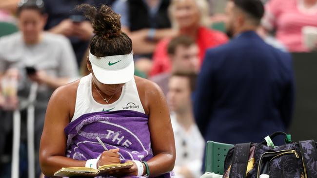 Naomi Osaka of Japan writes in a journal following defeat against Emma Navarro of United States. (Photo by Sean M. Haffey/Getty Images)