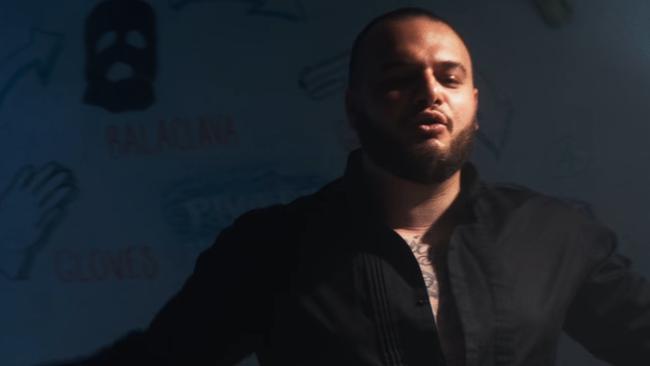 Ali "Ay Huncho" Younes stands in front of a whiteboard with writing about a gangland hit in a music video.