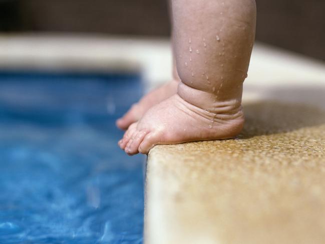 Feet of toddler standing on the very edge of a swimming pool, demonstrating water safety.