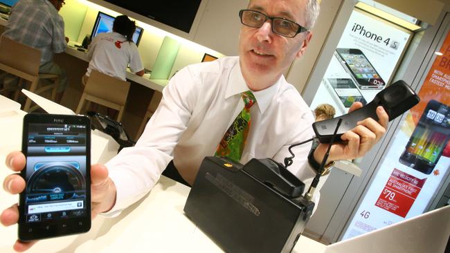 Telstra's Noel Hunt shows a modern phone alongside the first mobile phone (right) sold in 1987. It weighed 10kg and its battery lasted only 15 minutes.