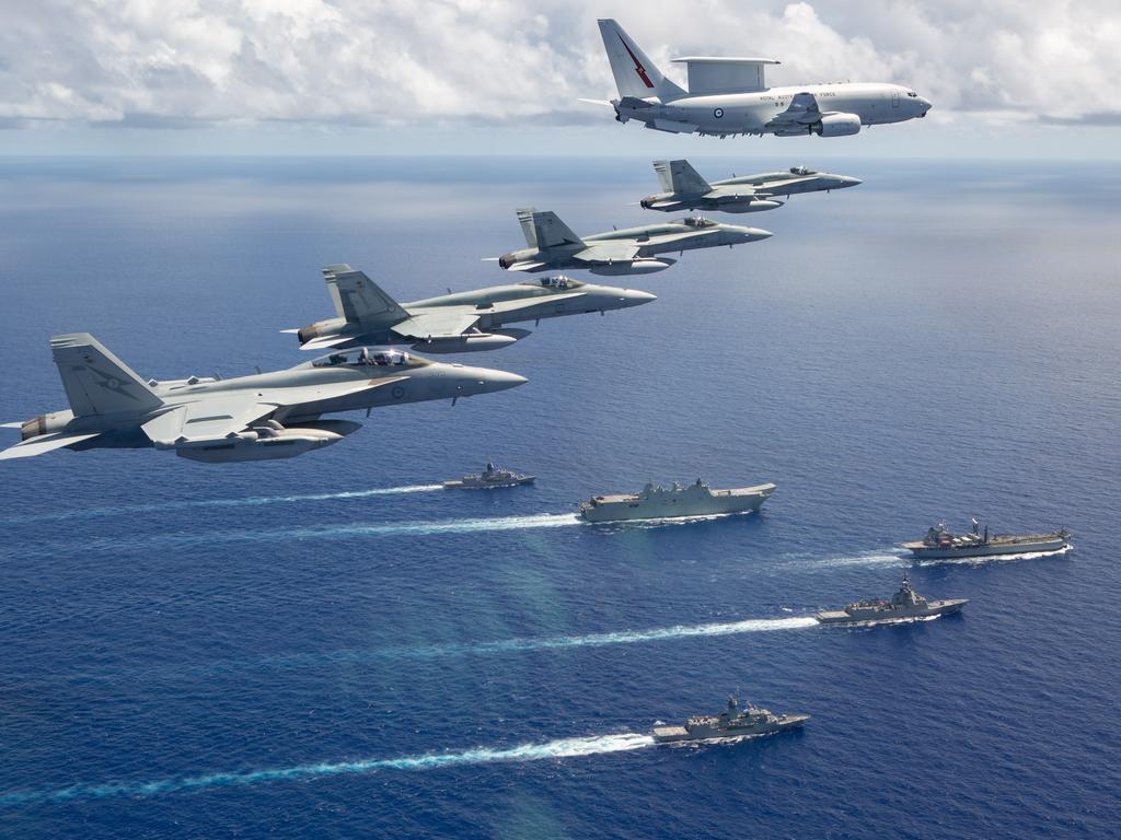 An E-7A Wedgetail from No. 2 Squadron, three F/A-18A Hornets from No. 77 Squadron and an EA-18G Growler from No. 6 Squadron fly over a navy task group of HMAS Canberra, Hobart, Stuart, Arunta and Sirius.