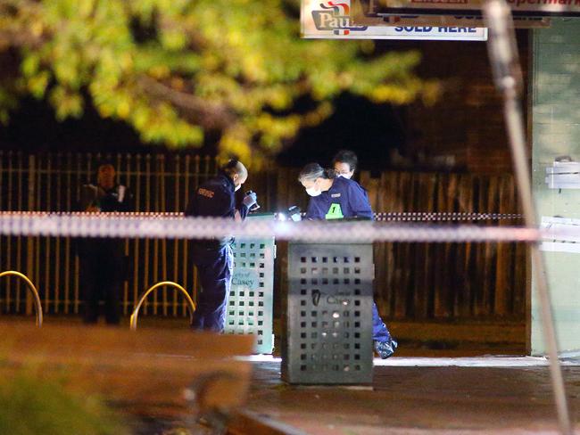 Forensics officers examine rubbish bins in front of the milk bar. Photo: Patrick Herve