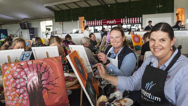 Caitlin Isaac (left) and Malinda Jones participate in the World's Largest Paint and Sip Luncheon for Momentum Mental Health at Clifford Park racecourse, Friday, June 21, 2024. Picture: Kevin Farmer