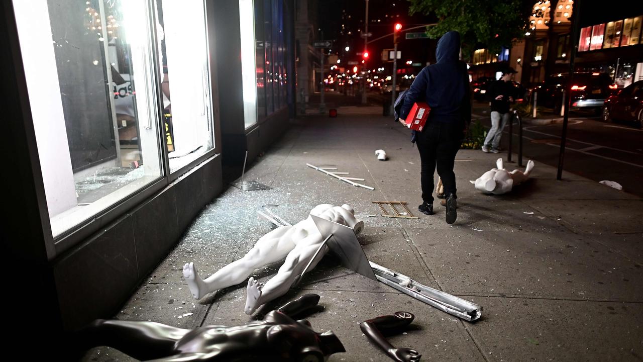 Mannequins lie on the footpath outside a looted shop while a hooded person walks past with a new pair of shoes. Picture: Johannes Eisele / AFP