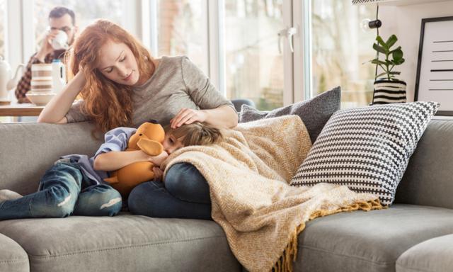 Mother taking care of sleepy child while sitting on couch in the living room