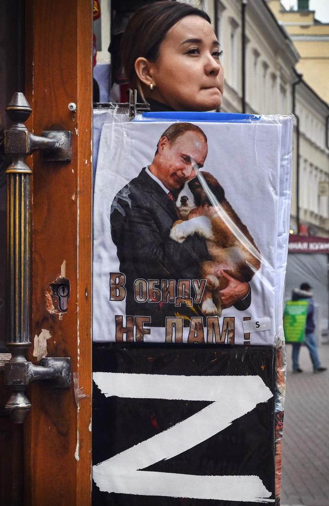 A vendor looks out of her gift shop in central Moscow on May 17, 2022, next to T-shirts bearing the letter Z, a tactical insignia of Russian troops in Ukraine, and a picture of Vladimir Putin. Picture: Alexander Nemenov/AFP