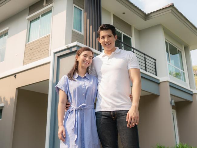 Portrait of young couple standing and hugging together looking happy in front of their new house.  home loan generic