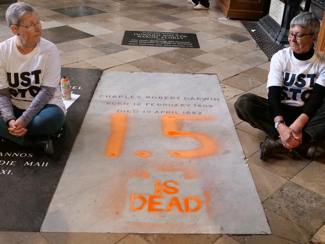 A handout picture taken and released by the Just Stop Oil climate campaign group on January 13, 2025, shows two activists, sitting on the floor alongside the grave of Charles Darwin, after they sprayed "1.5 is dead" over it in protest against climate change in action, inside Westminster Abbey in central London. Activists Alyson Lee and Di Bligh from the Just Stop Oil group on Monday painted inscriptions on the grave of famous naturalist Charles Darwin in to protest against political inaction on global warming. In a video posted by the group on X, two activists were seen writing in orange paint "1.5 is dead", a reference to the 1.5Â°C limit on global warming set by the international Paris climate agreement. (Photo by JAMIE LOWE / Just Stop Oil / AFP) / RESTRICTED TO EDITORIAL USE - MANDATORY CREDIT "AFP PHOTO /  JUST STOP OIL / Jamie Lowe " - NO MARKETING - NO ADVERTISING CAMPAIGNS - DISTRIBUTED AS A SERVICE TO CLIENTS