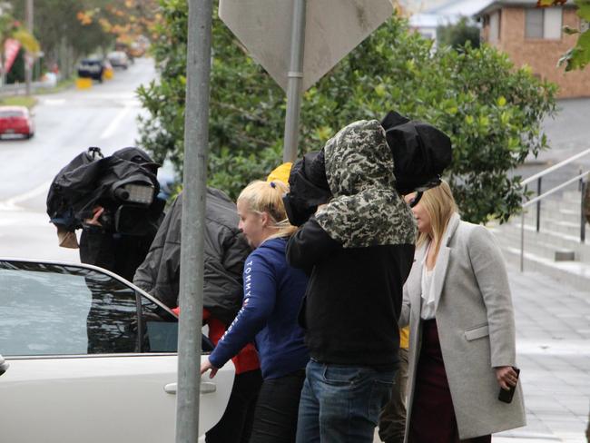 The woman (orange shirt) covers her face as she gets into a car at Wyong Local Court after her first court appearance in 2020. Picture: Fiona Killman