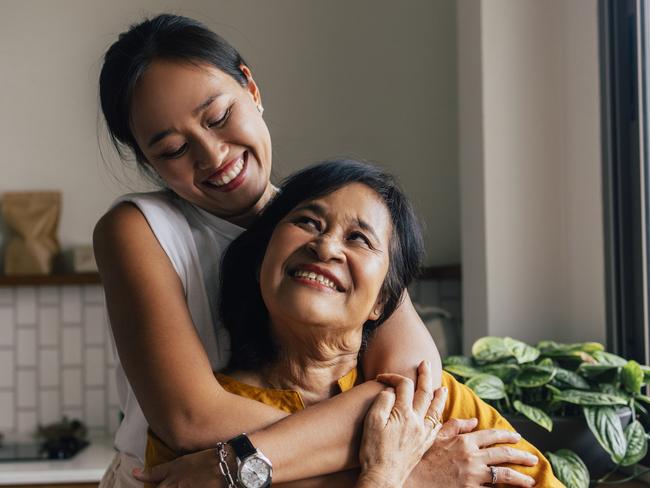 Portrait of Asian family of two, mother and daughter, sitting in a kitchen, daughter hugging her mother with a lot of love and devotion.