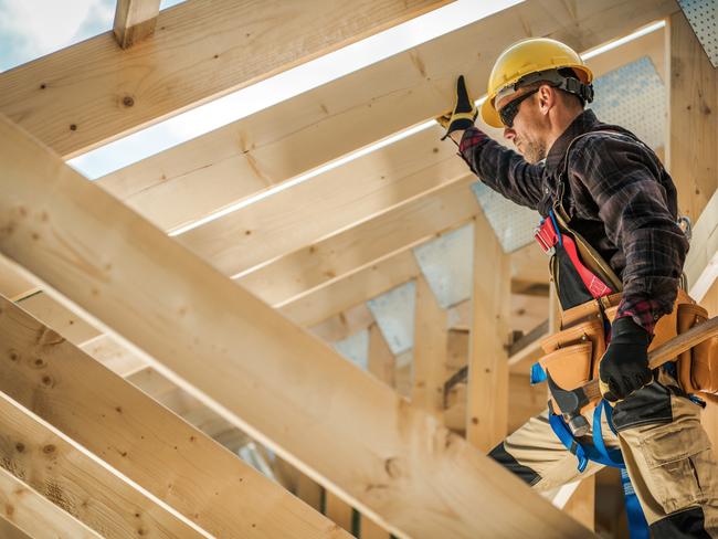 Construction Worker on Duty. Caucasian Contractor and the Wooden House Frame. Industrial Theme.