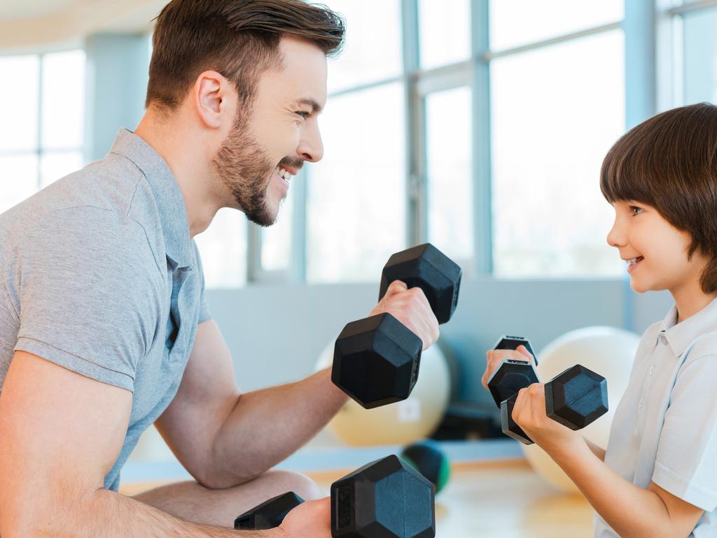 Happy father and son exercising with dumbbells and smiling while both standing in health club