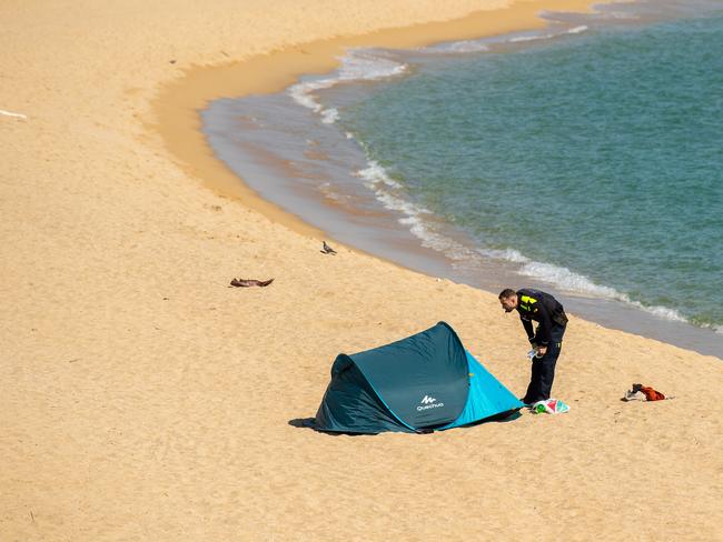 A metropolitan police officer clears a couple of tourists who slept on the beach after closing the access to La Mar Bella beach in Barcelona, Spain. Picture: Getty Images