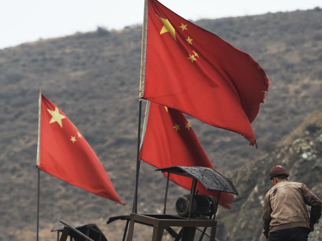 (FILES) This file photo taken on November 20, 2015 shows Chinese flags next to a worker clearing a conveyer belt used to transport coal, near a coal mine at Datong, in China's northern Shanxi province. - China's surprise pledge to slash its carbon footprint to zero by 2060 was met with cautious applause, but fresh spending on coal to rev up a virus-hit economy threatens to nullify its audacious bid to lead the world into a low carbon future. (Photo by GREG BAKER / AFP) / TO GO WITH coal-environment-pollution-China-climate,FOCUS by Poornima WEERASEKARA and Haomin LI