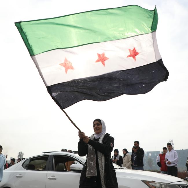 A woman waves the flag of the Syrian rebels as people gather to celebrate the fall of the government in Umayyad Square, Damascus.