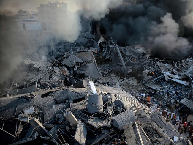 Smoke rises from a levelled building as people gather amid the destruction in the aftermath of an Israeli strike on Gaza City on October 26, 2023, as battles continue between Israel and the Palestinian Hamas group. (Photo by Omar El-Qattaa / AFP)