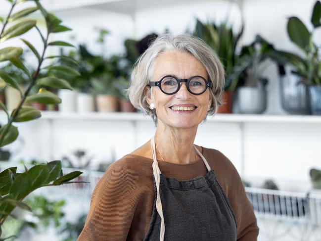 Portrait of senior female florist at small business flower shop. Happy mature woman wearing apron working in a small flower store; working in retirement happy retiree worker generic