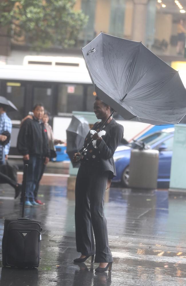 A worker in Sydney CBD struggles with her umbrella in the strong wind. Picture: John Grainger