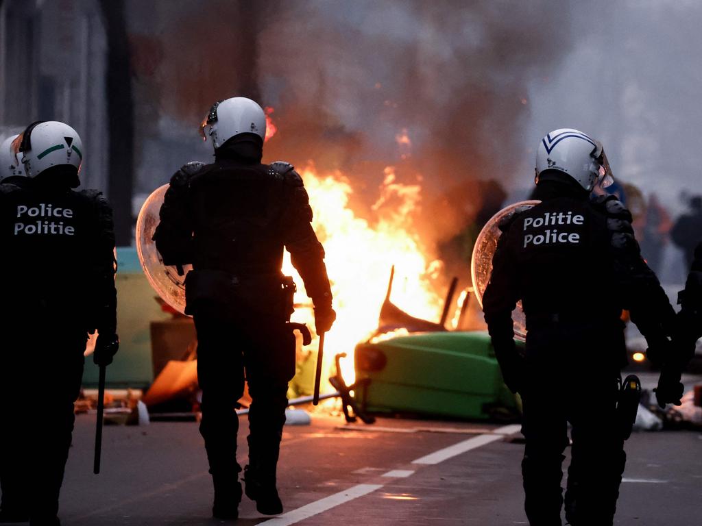 Belgian riot police walk past a burning bins as clashes erupt during the Brussels demonstration.