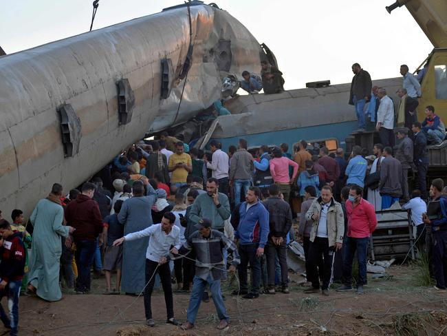 People gather around the wreckage of two trains that collided in the Tahta district of Sohag province, some 460 kilometres (285 miles) south of the Egyptian capital Cairo, reportedly killing at least 32 people and injuring scores of others, on March 26, 2021. - Egypt has been plagued with fatal train accidents in recent years that have been widely blamed on crumbling infrastructure and poor maintenance. (Photo by - / AFP)