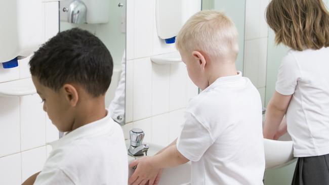 Children standing in line washing their hands in a primary school bathroom