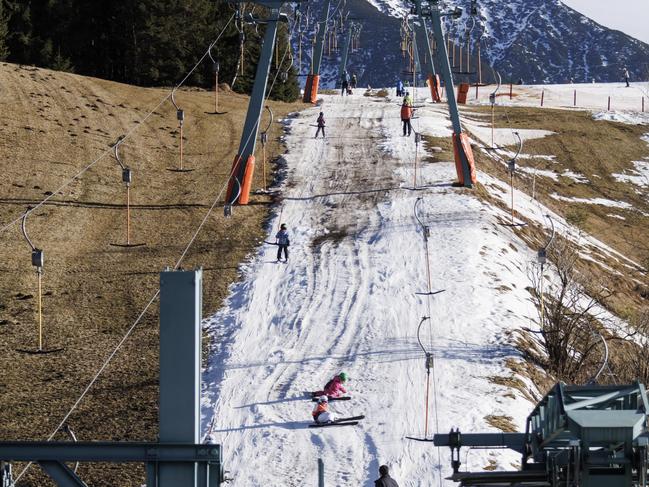 Skiers ride a ski lift on a track covered in artificial snow, while grass covers the rest of the hill on January 7, 2023 in Seefeld, Austria. Alpine ski resorts in Austria, Germany and Switzerland faced an unusually warm January. Picture: Jan Hetfleisch/Getty Images