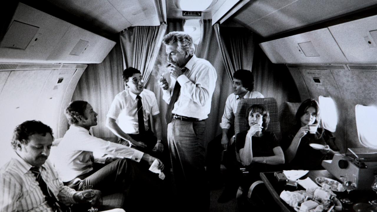 Bob Hawke surrounded by advisors and media (L-R) journalist Colin Parks, Senator Kerry Sibraa, journalist Peter Logue, senior advisor Geoff Walsh, staffers Kate Moore and Janet Willis, lights up a cigar on a VIP flight during the 1983 Federal Election Campaign. Picture: Ray Strange.