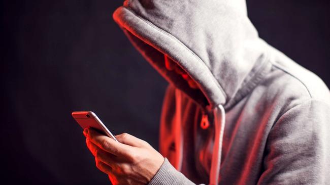 Man wearing hoody sweater with mobile phone in hands. Crime and hacking concept; scam generic.