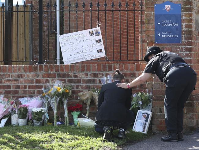 A mourner is comforted by a police officer as flower tributes are placed at the school where victim James Furlong taught. Picture: AP