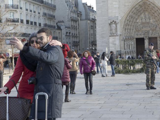 A tourist couple takes a photograph in front of the Notre Dame cathedral in Paris as French soldiers patrol, Saturday, Jan. 17, 2015. Tourism officials couldn’t give figures of the number of sightseers in the immediate aftermath of the terrorist attacks that killed 17 people in Paris, but visits by The Associated Press to major sites and interviews with vendors indicated an initial drop in visitors. Among the tourists that were still braving visits, many took comfort in the extra security presence. With 10,500 troops deployed across the country, including 6,000 in the Paris region alone, the security operation put in motion after the attacks is the most extensive on French soil in recent history. (AP Photo/Jacques Brinon)