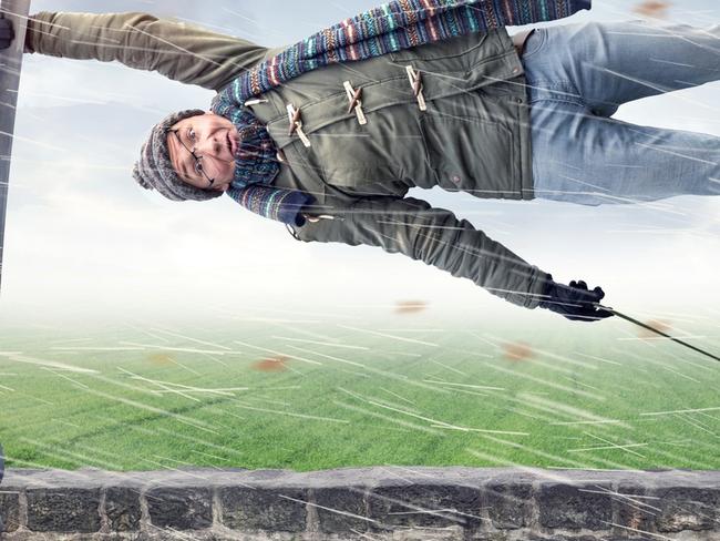 Man flying away horizontally in a storm while holding on to a street lamp with one hand. The other hand is holding an upended umbrella. Istock