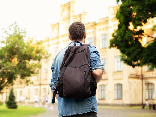 Student university standing with his back to the camera and his backpack on one shoulder and walking in university campus, education concept. Young man walking down street with a backpack. Back view.